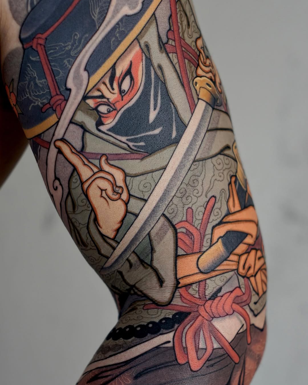 Colorful leg tattoo featuring an Asian-inspired figure with ornate clothing, ribbons, and floral elements in red, gold, navy, and cream tones.