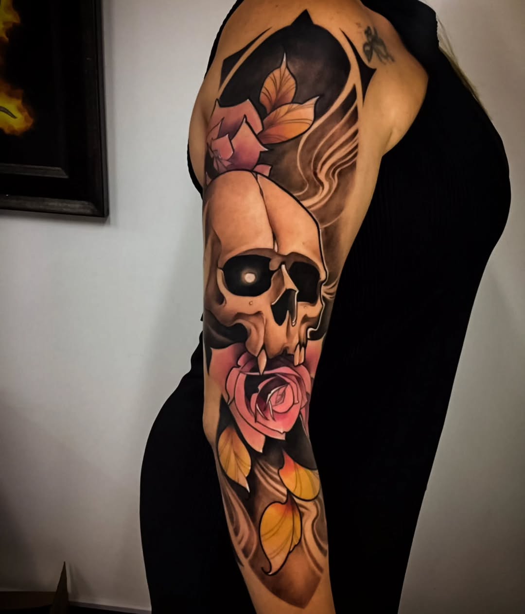 Full-sleeve arm tattoo featuring a skull with roses and flowing hair elements in orange, pink, red, and black colors.