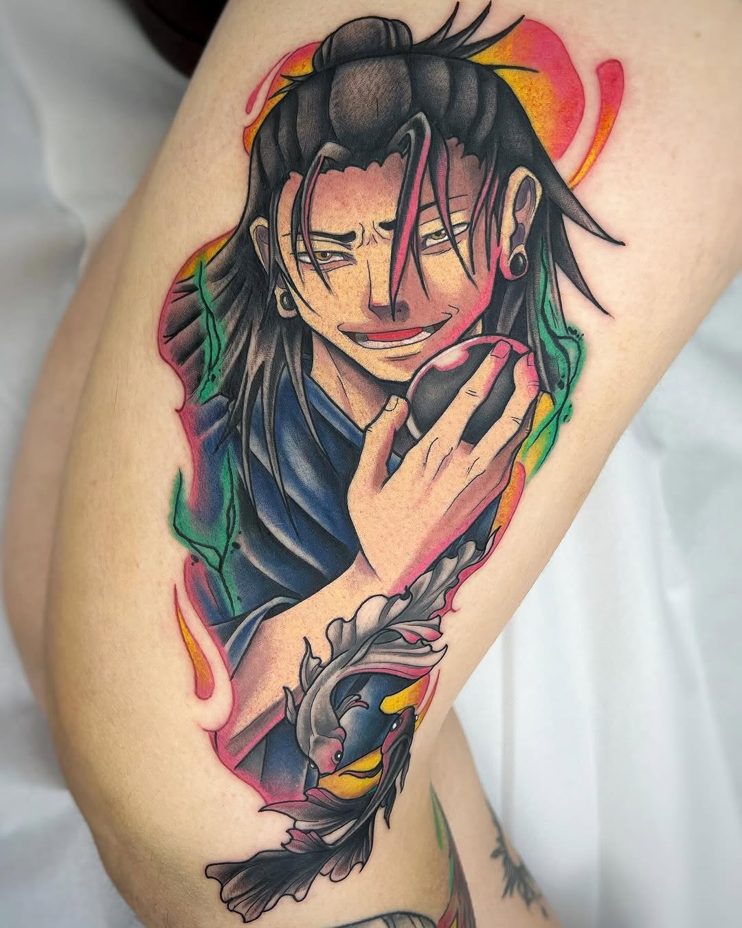 Colorful portrait tattoo of a long-haired character with a smiling expression, wearing dark clothing, placed on the upper leg with vibrant pink, yellow, green, and blue background elements.