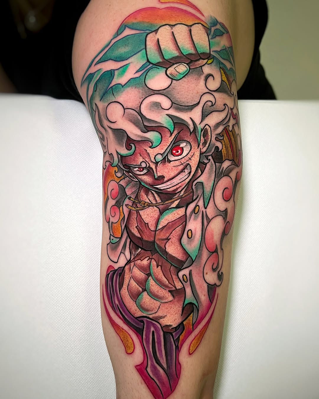 Colorful leg tattoo featuring a demonic face with red eyes, surrounded by swirling clouds and flames in red, green, orange, and purple tones.