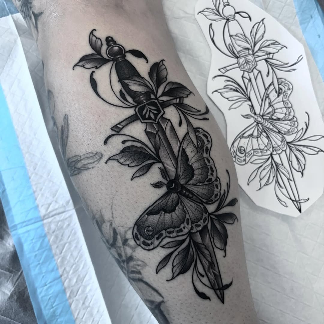 Black ink tattoo on upper arm featuring two moths with detailed wings perched on ornate flowering plants with leaves.