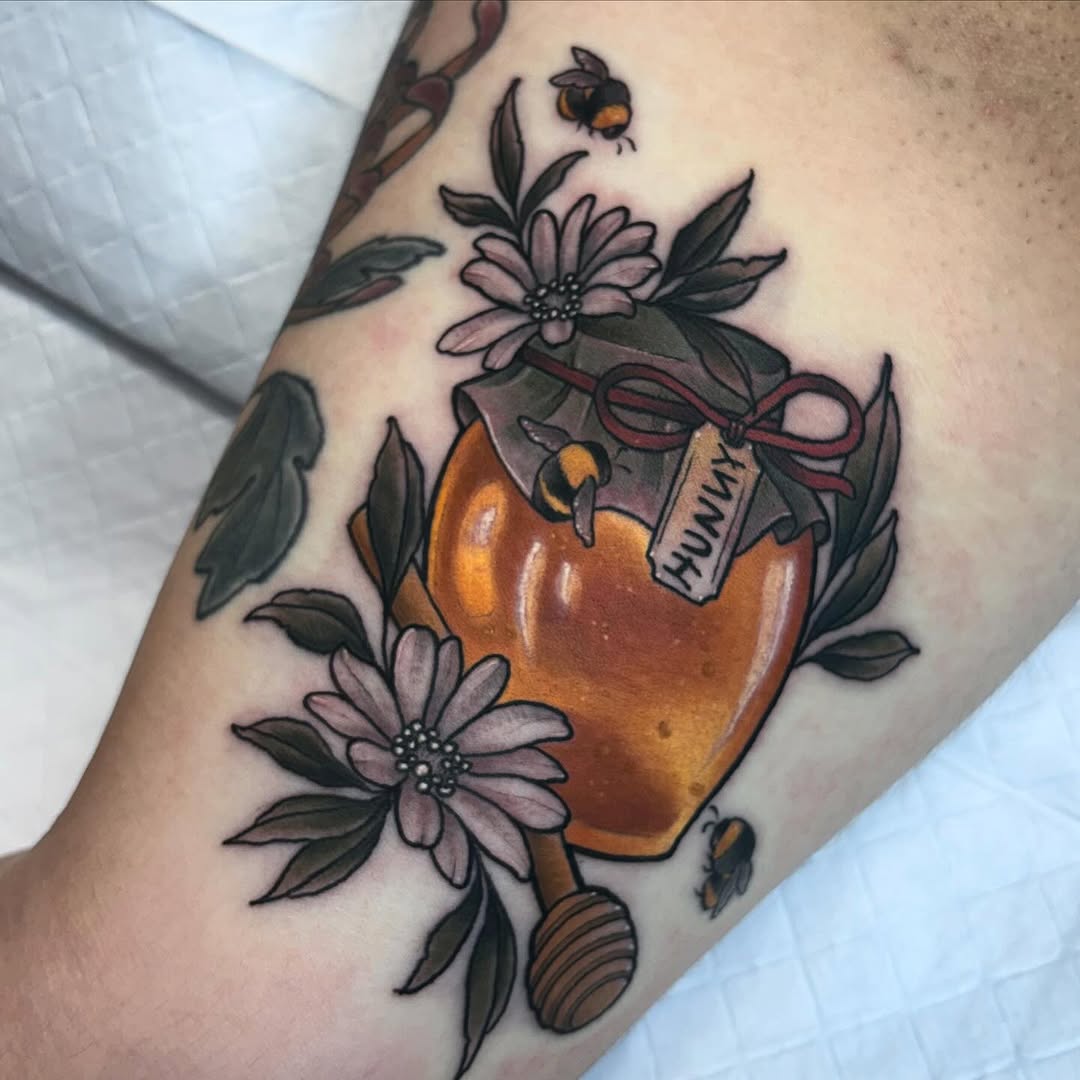Honey jar tattoo with pink and purple flowers, green leaves, bees, and a burgundy bow on the upper arm.