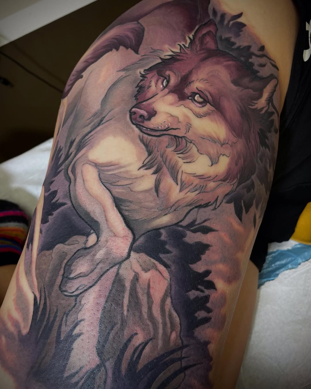 Colorful wolf head tattoo on upper arm featuring purple and pink tones with detailed facial features and fur texture.