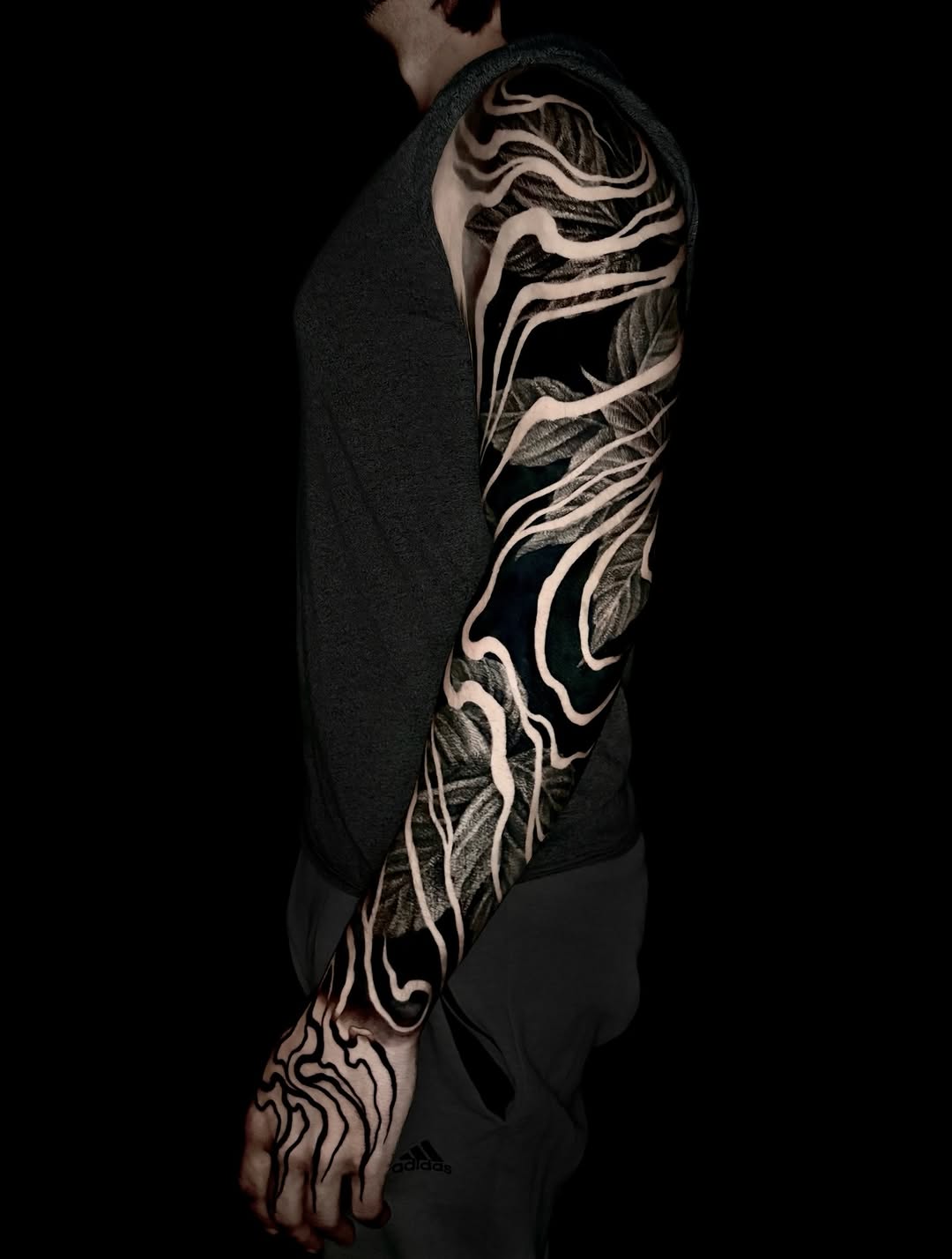 Full-sleeve arm tattoo featuring organic flowing lines and leaf motifs in black and white ink on a person wearing dark clothing.