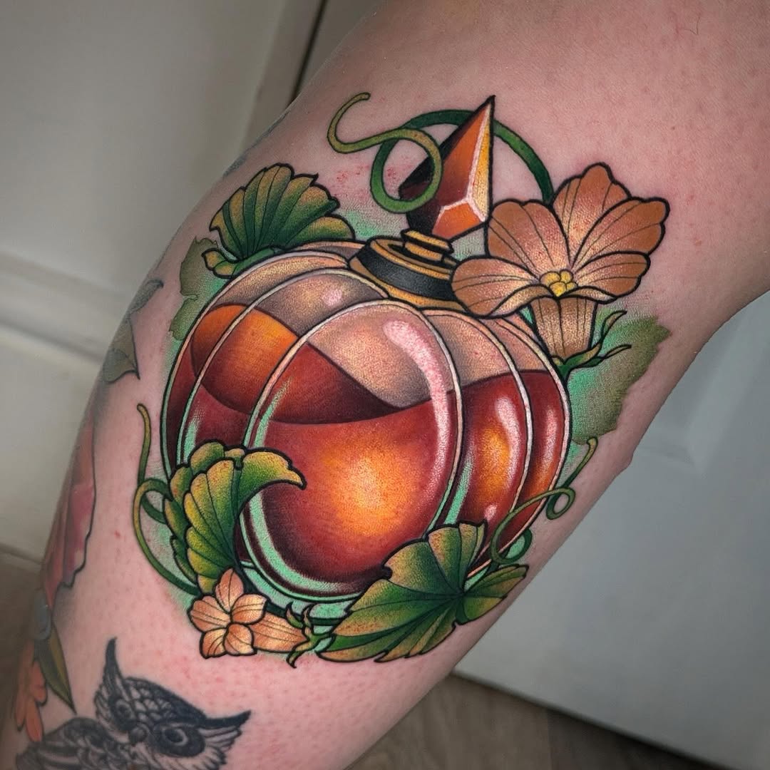 Colorful tattoo on an arm featuring a glowing red and orange orb surrounded by green vines, orange flowers, and a small hat with a feather on top.