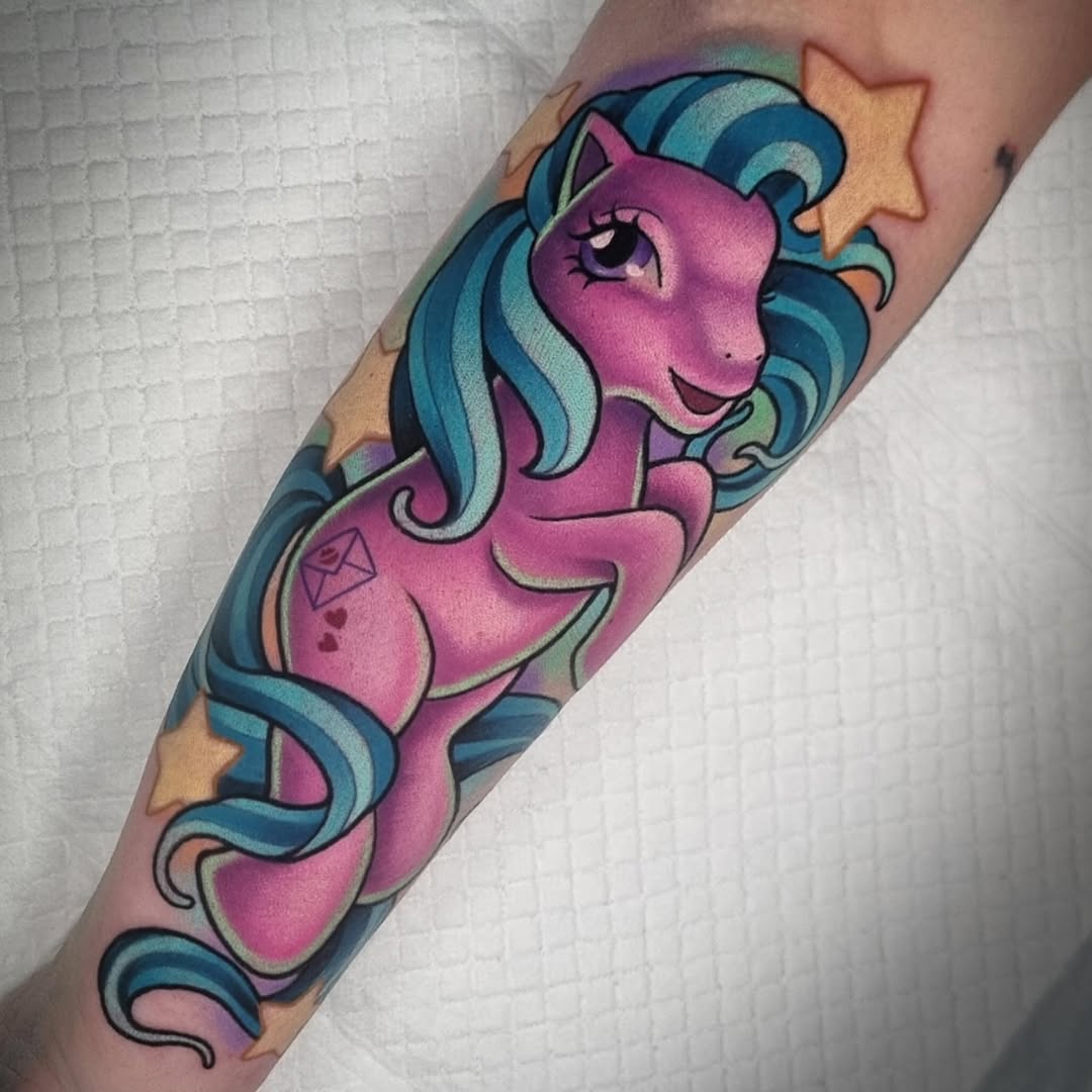 Pink unicorn with blue and teal mane and tail, gold stars, and small geometric designs on the foreleg, tattooed on the inner arm.