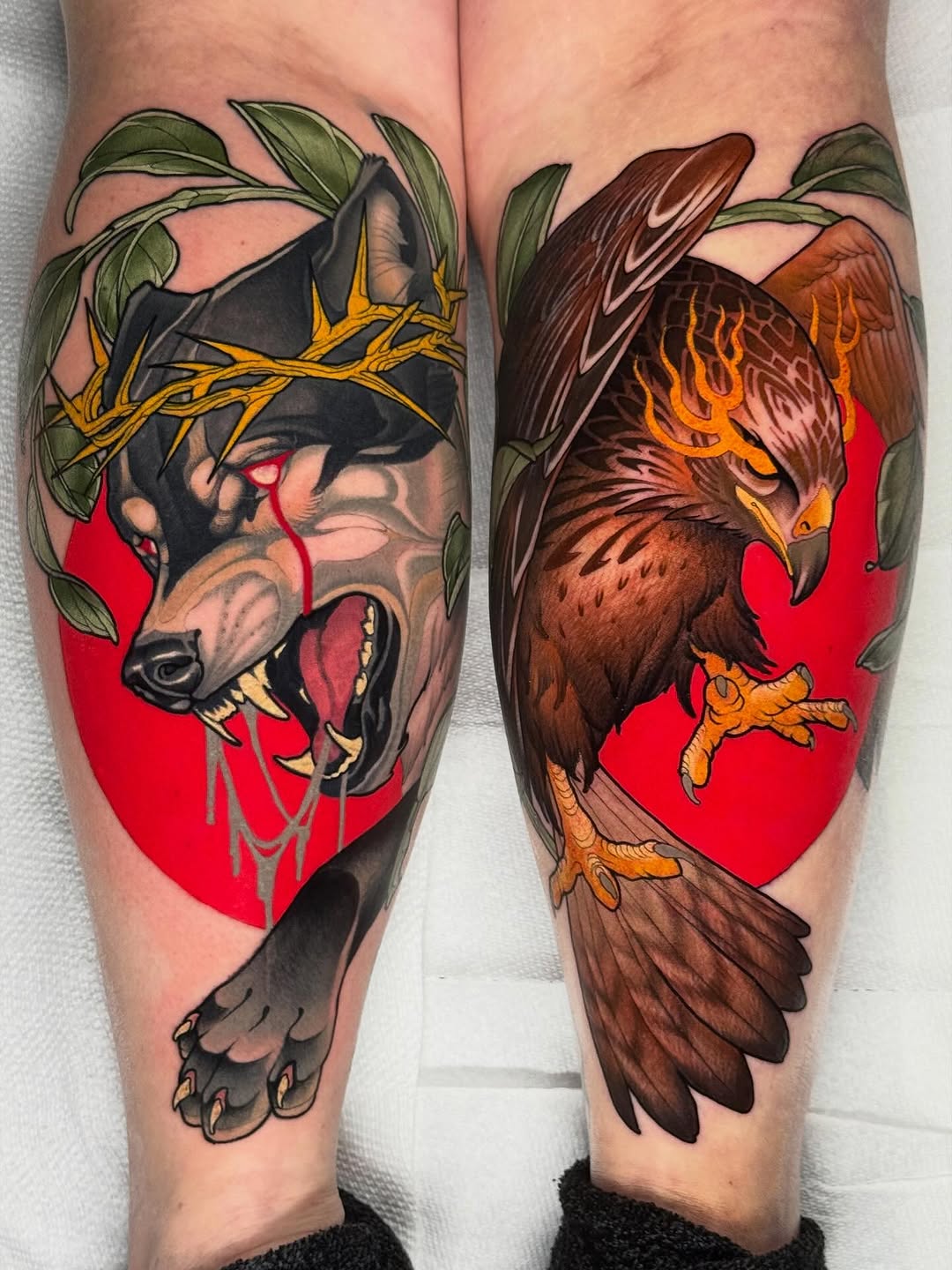 Pair of calf tattoos featuring a snarling deer head and an eagle with red backgrounds and green foliage, rendered in brown, gold, and black ink.