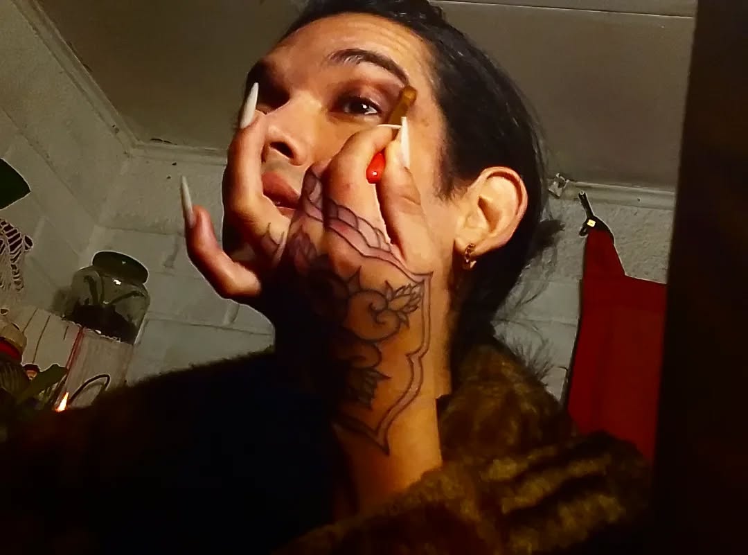 Facial tattoo featuring anatomical line work on the cheek and neck in black ink with red accents on the nails.