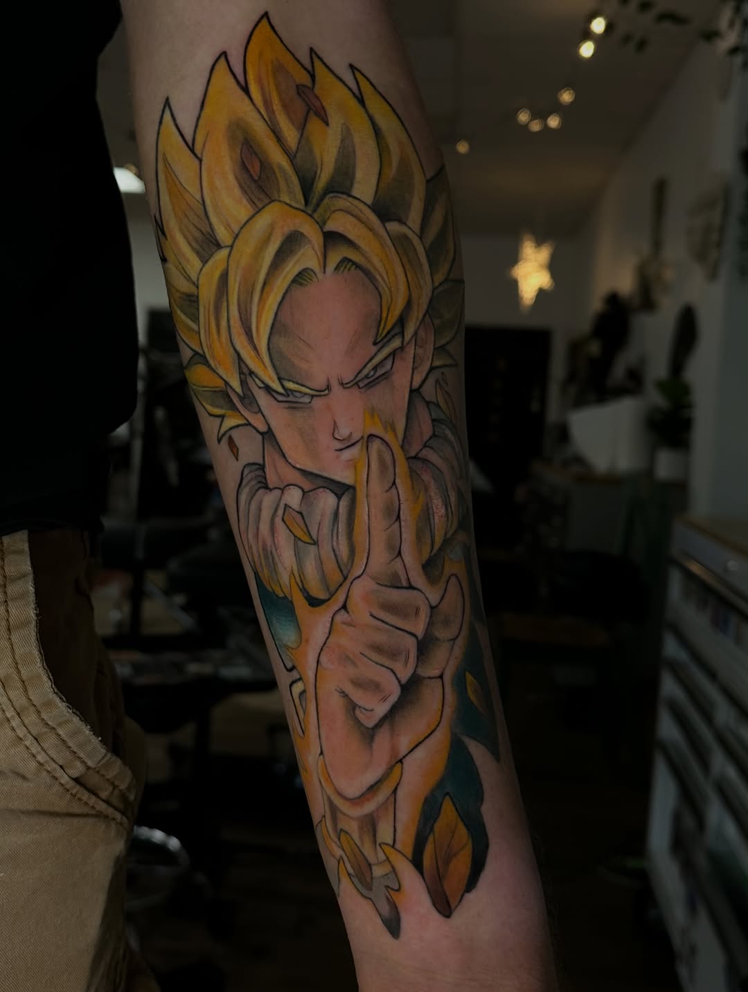 Blonde-haired character with spiky hair and muscular build tattoo on forearm in gold, orange, and flesh tones with black outlines.