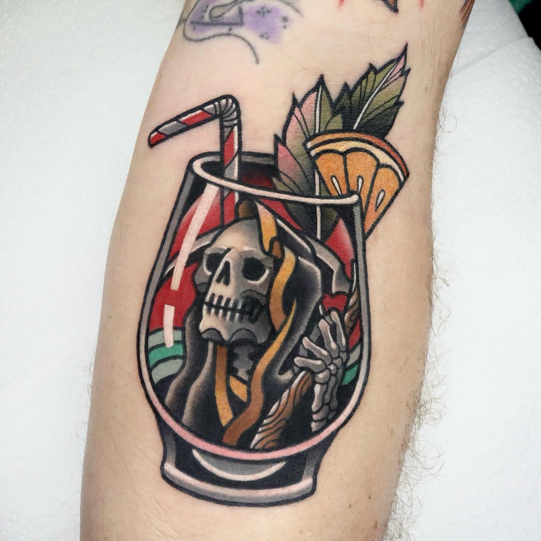 Colorful tattoo on an arm featuring a skull inside a cocktail glass with a straw, tropical leaves, and a striped rim in red, orange, yellow, and green.