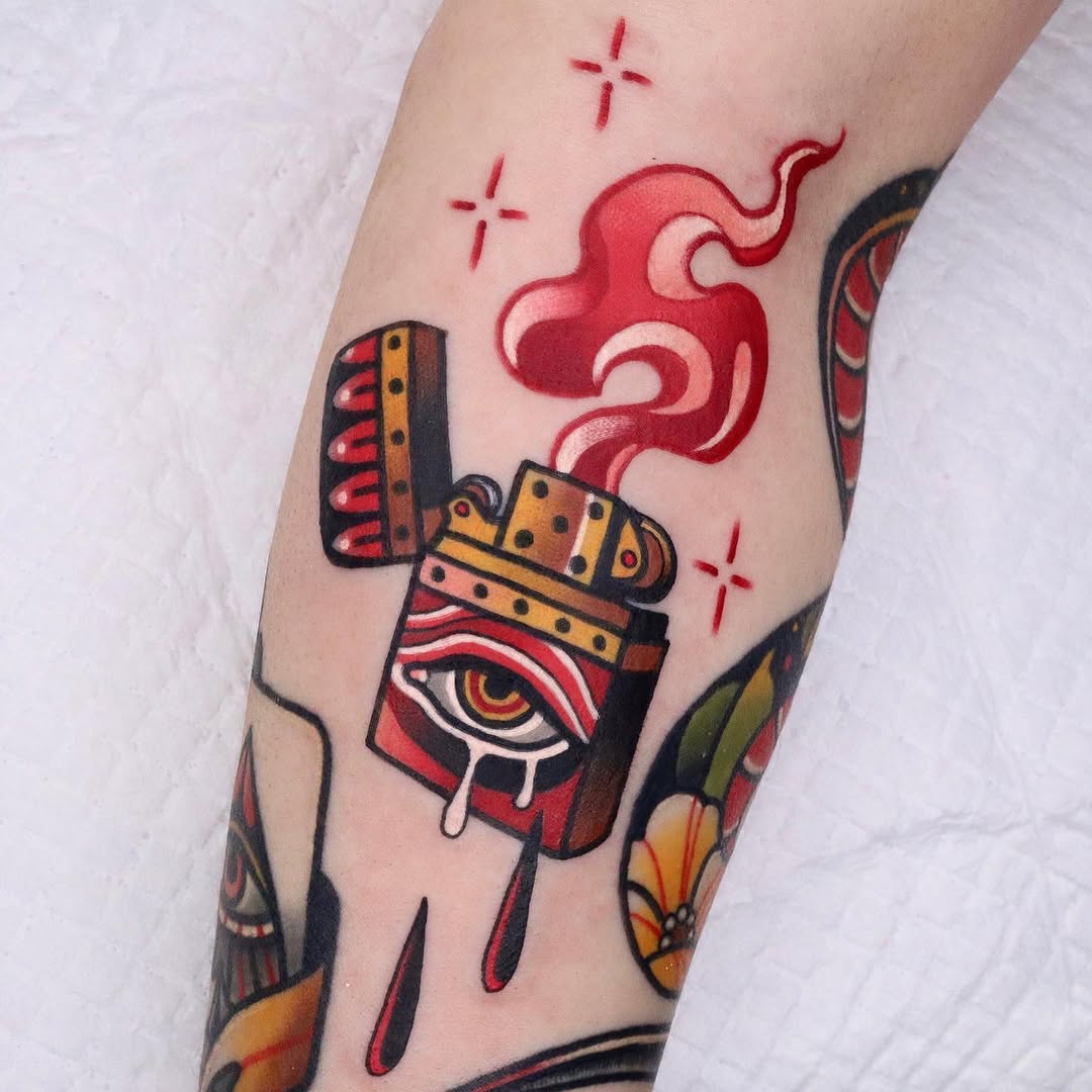 Colorful lighter tattoo with an eye and flame design on the upper arm, surrounded by red cloud motifs and small crosses in red ink.