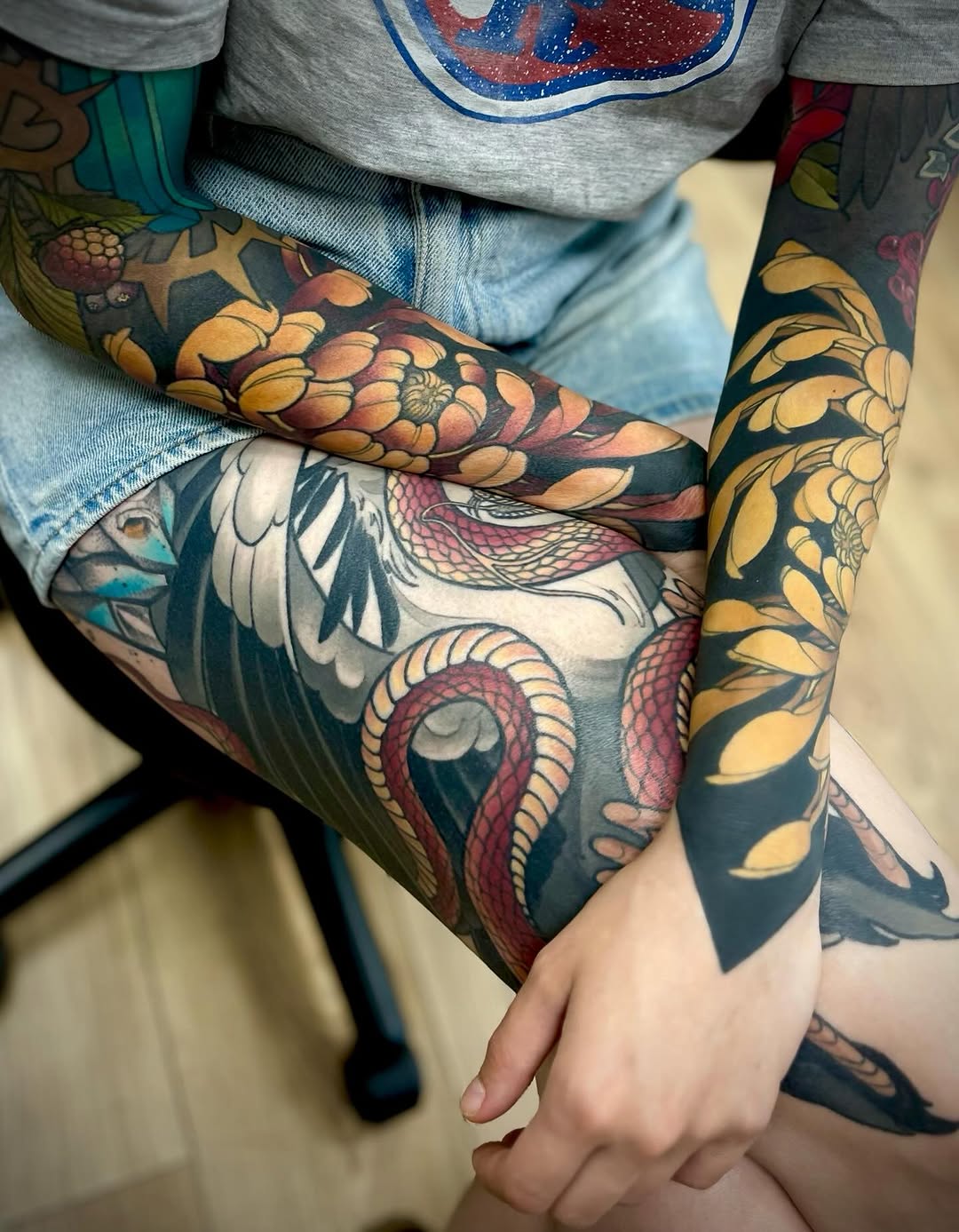 Colorful arm tattoo featuring a fish with detailed scales, a bird with extended wings, and golden floral elements on dark background.