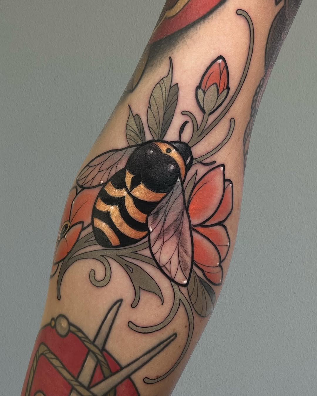 Bee with black and golden-yellow striped body and translucent wings surrounded by red flowers and ornamental scrollwork on an arm.