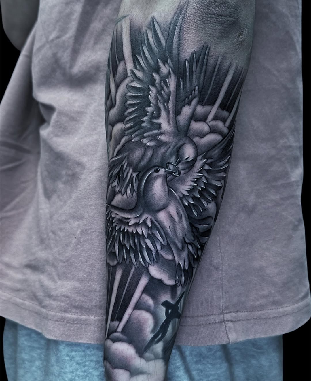 Detailed winged bird tattoo on forearm rendered in shades of gray and black ink, showing intricate feather work and dimensional shading.