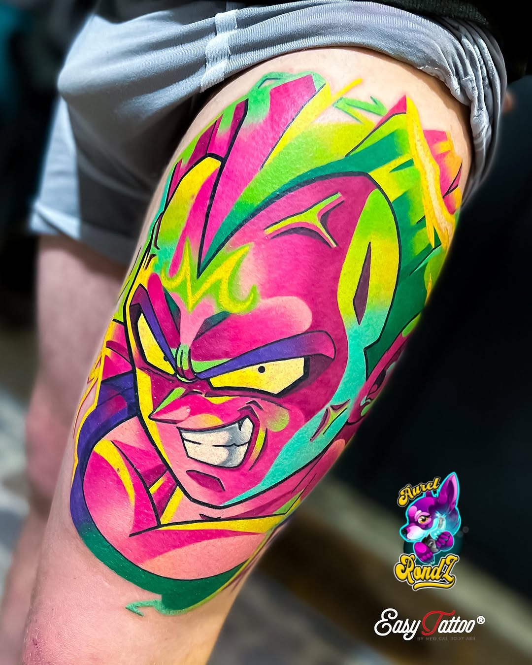 Colorful abstract face tattoo on upper thigh featuring bright pink, yellow, green, and blue geometric shapes with bold black outlines.