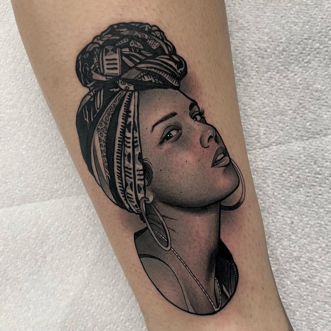 Profile portrait of a woman with an ornate wrapped head covering featuring geometric patterns, shown on an upper arm in black ink with shading.