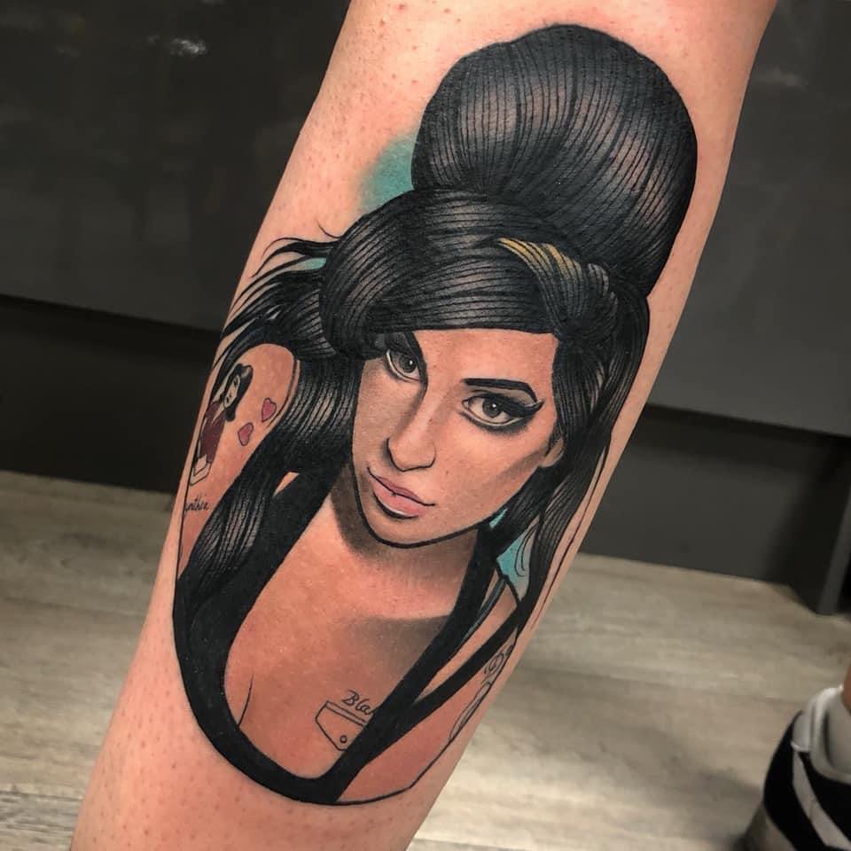 Portrait tattoo of a woman with black hair in a bun and headband on the upper leg, featuring pink lips and a light blue background accent.