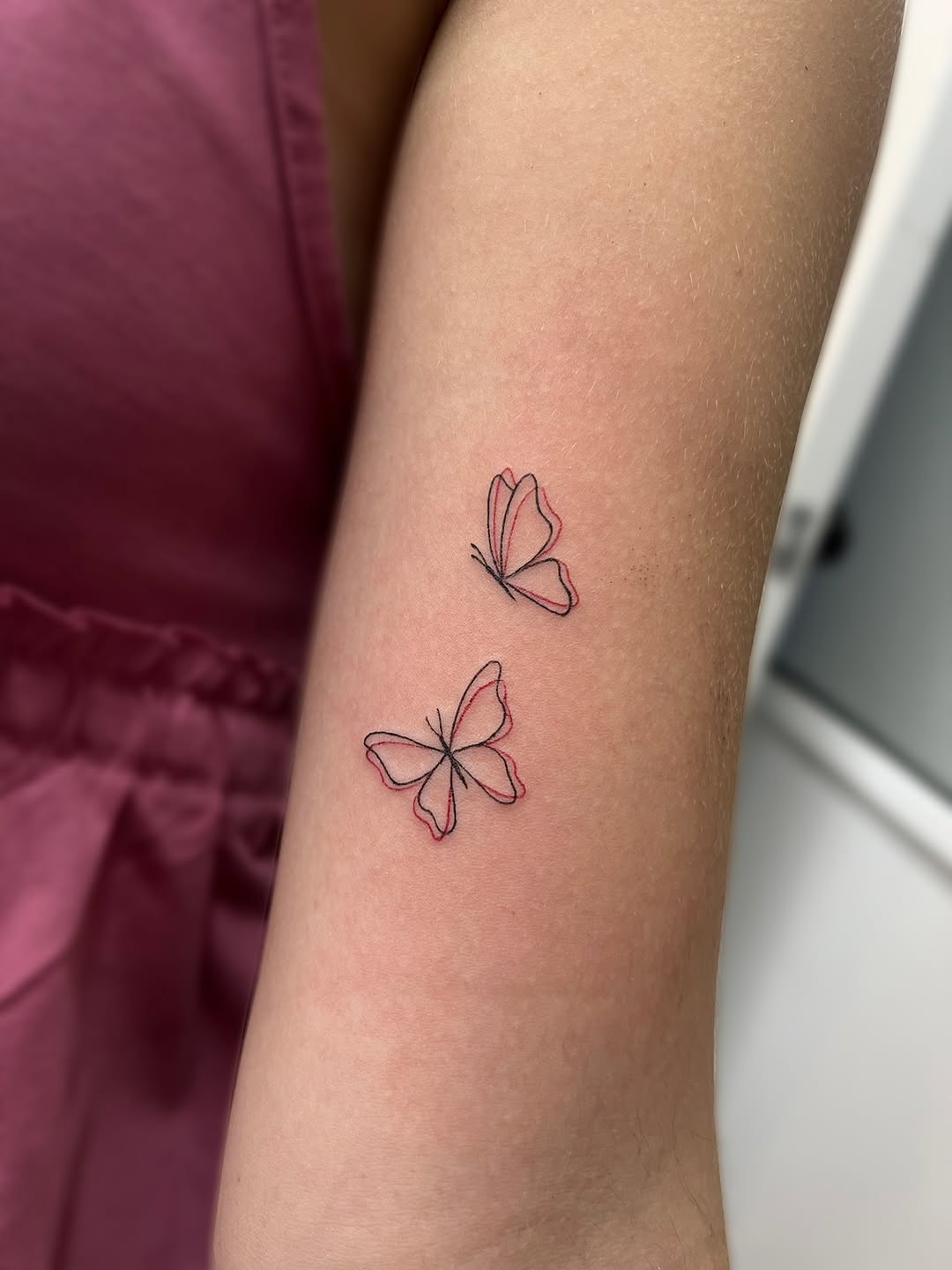 Two delicate butterflies with outlined wings in red and black ink on the forearm.