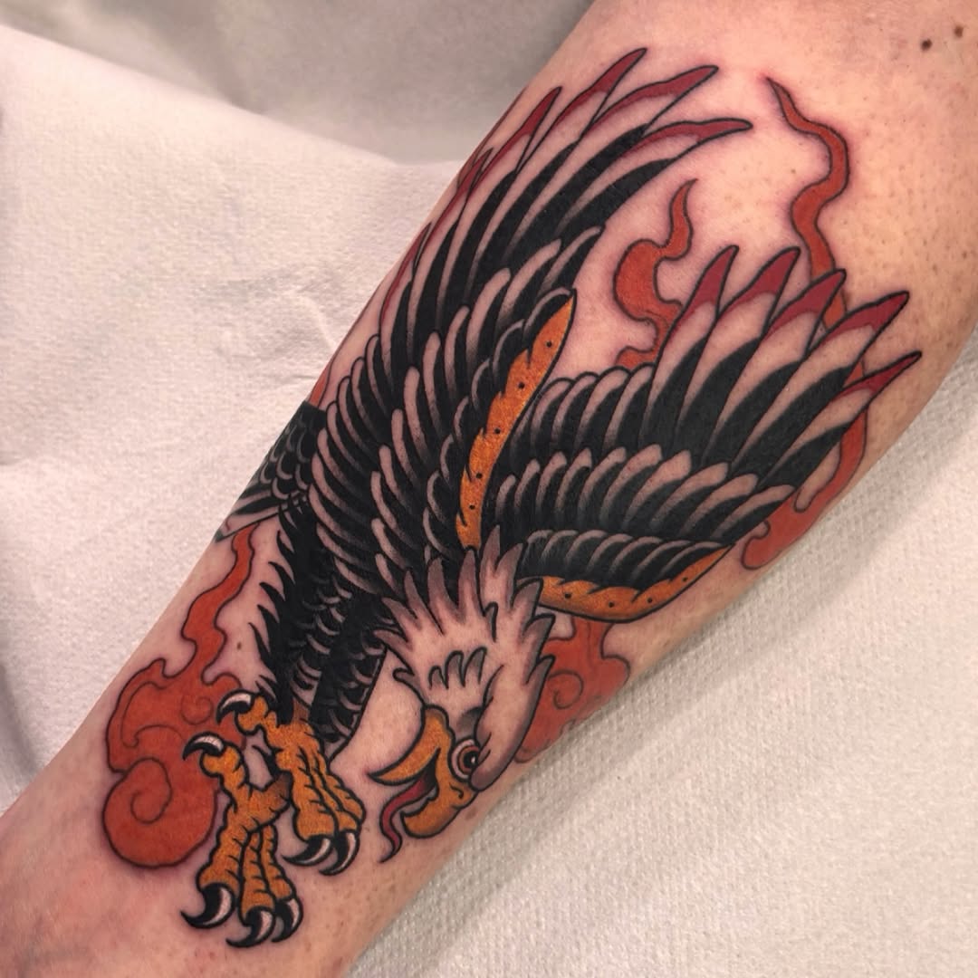 A phoenix tattoo with black wings, orange and red flames, and detailed talons on a person's forearm.