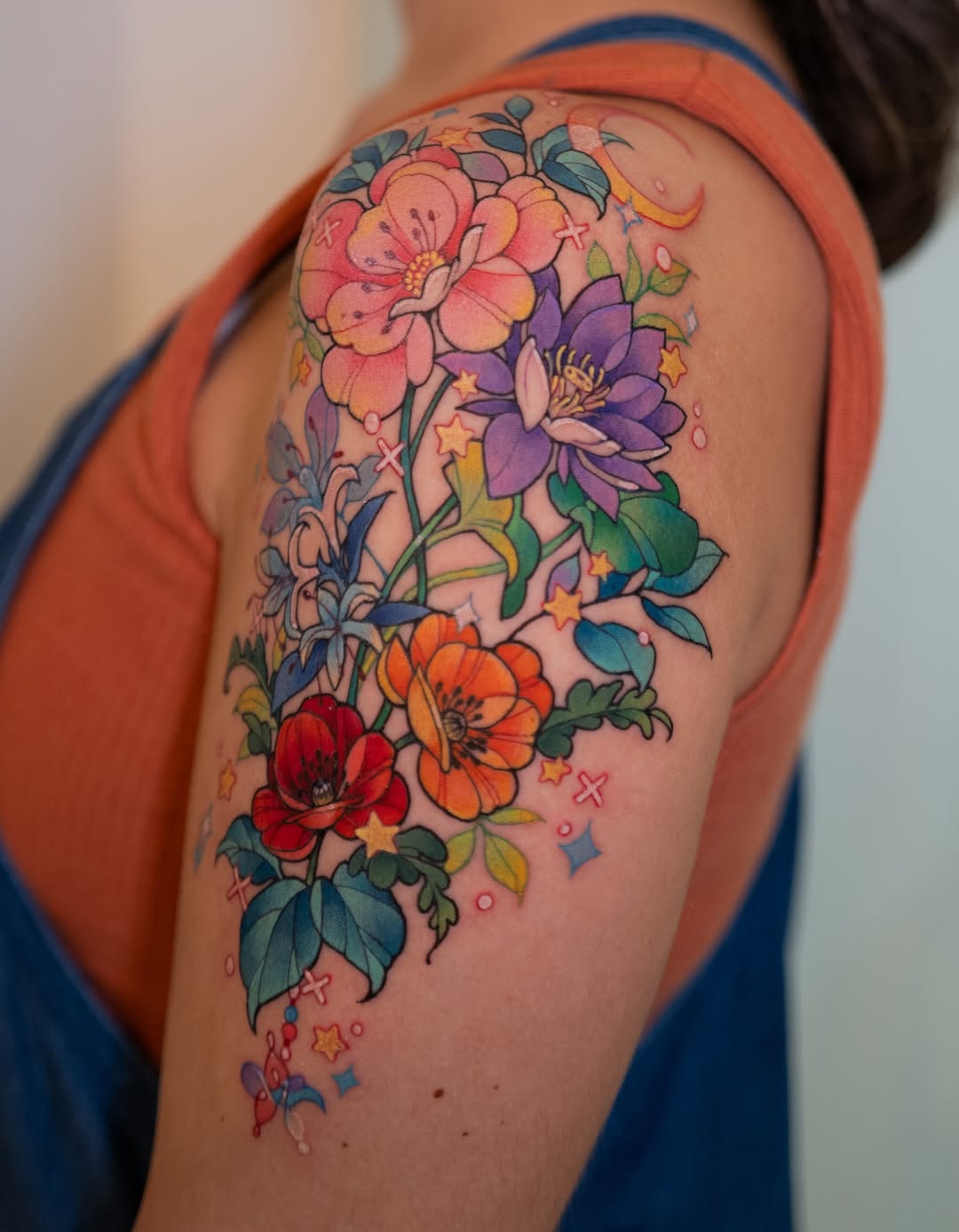 Colorful floral tattoo on upper arm featuring pink, purple, orange, and red flowers with green leaves and small stars in a vertical arrangement.