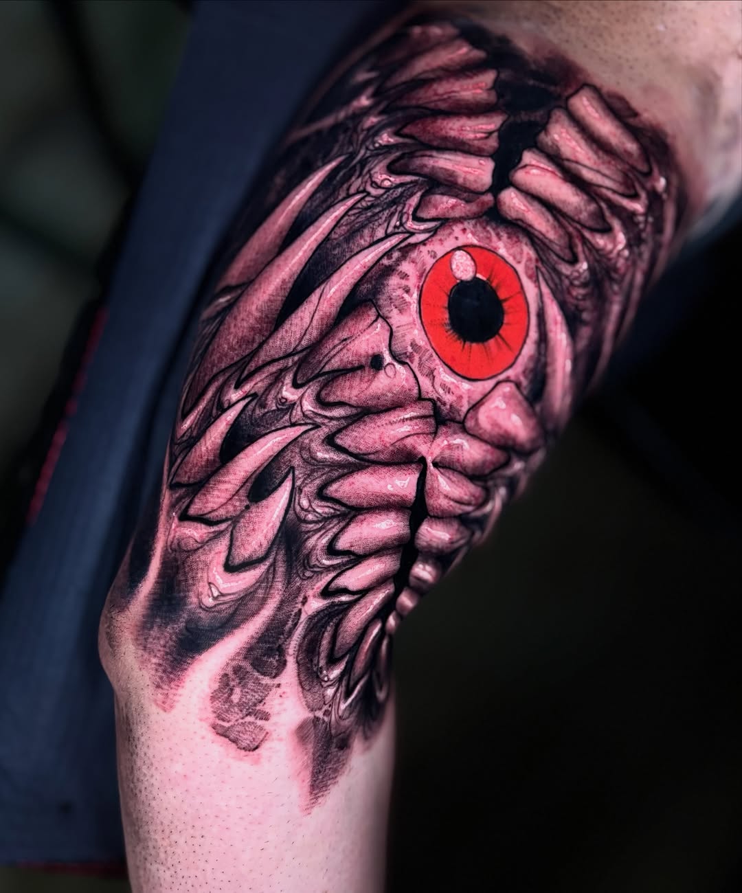 Anatomical skeleton wing with a striking red iris eye tattoo on the upper arm, rendered in pink and black ink.