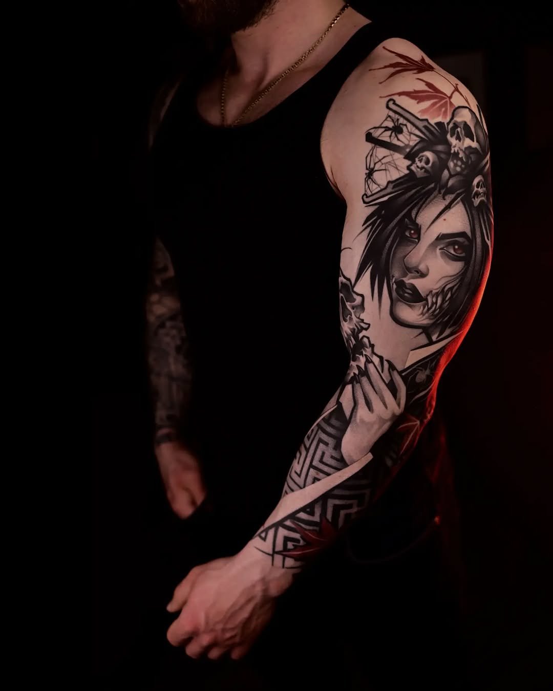 Full sleeve tattoo featuring a woman's face, skulls, bamboo, and geometric patterns in black ink on the upper arm and forearm.