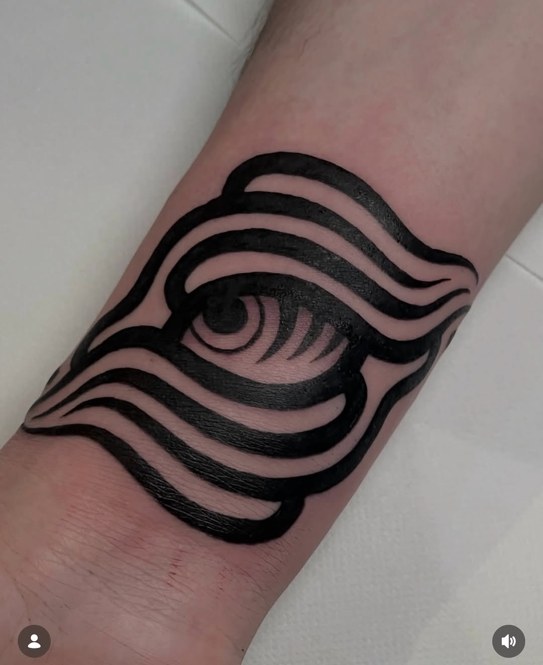 Bold black eye tattoo with wavy horizontal lines framing the design, positioned on the inner forearm with solid fill and sharp linework.