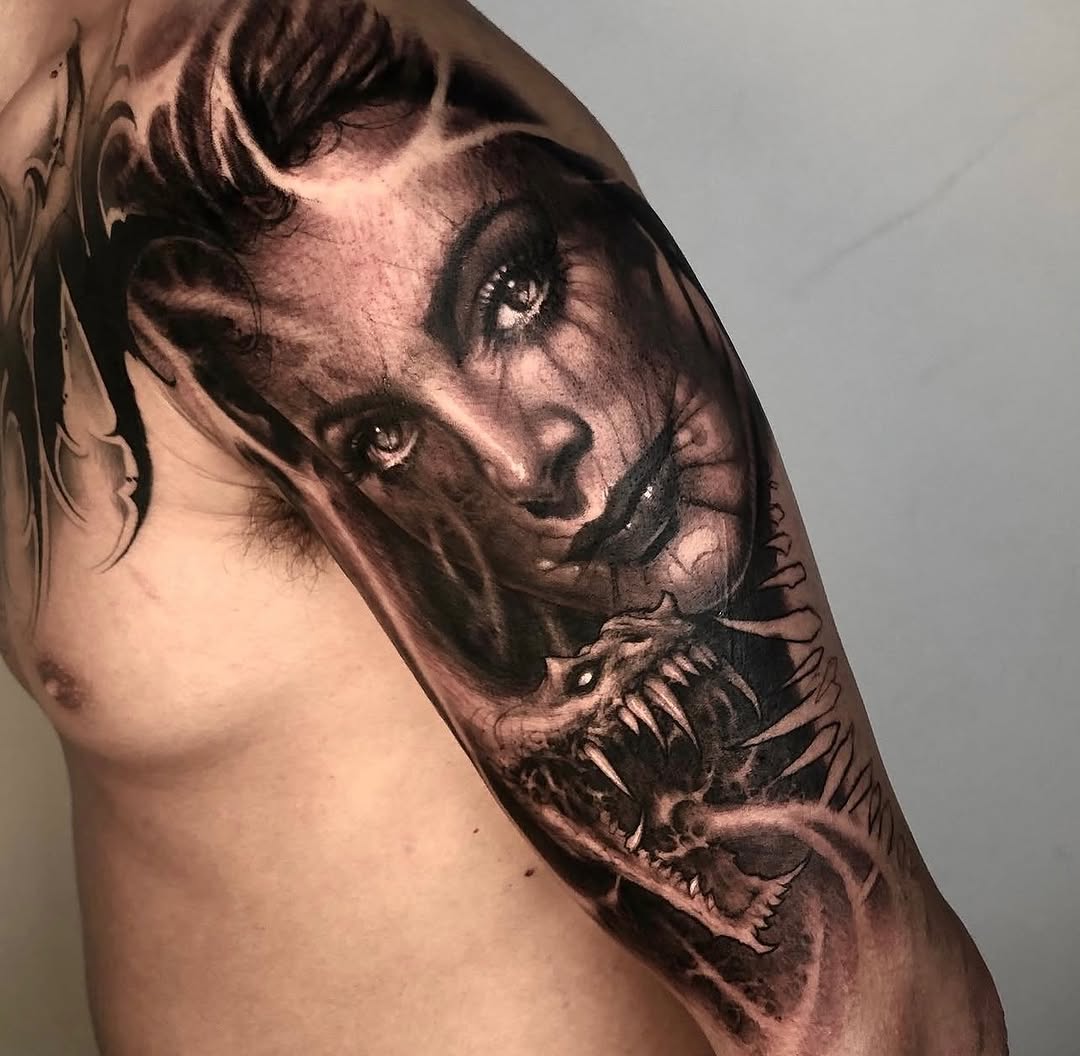 Detailed portrait tattoo on upper arm depicting a woman's face with dramatic eyes and a demon or creature below, rendered in brown and black tones.