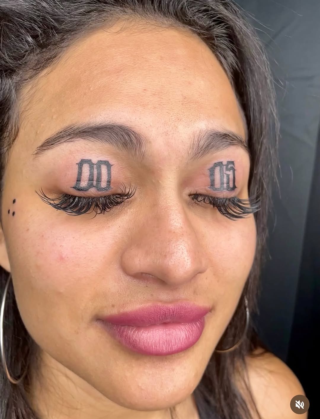 Closed eyelids with Roman numerals tattooed on each lid and false lashes applied, displayed in a portfolio photo.