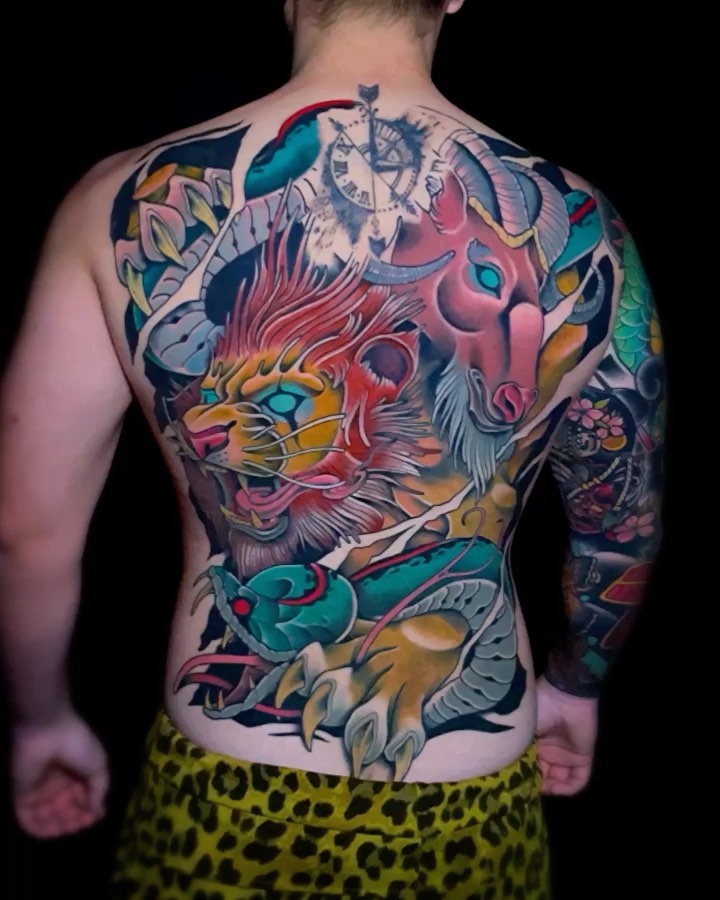 Colorful back tattoo featuring a red and gold dragon with elaborate feathers, surrounded by blue and teal serpents, flowers, and decorative elements in vibrant hues.