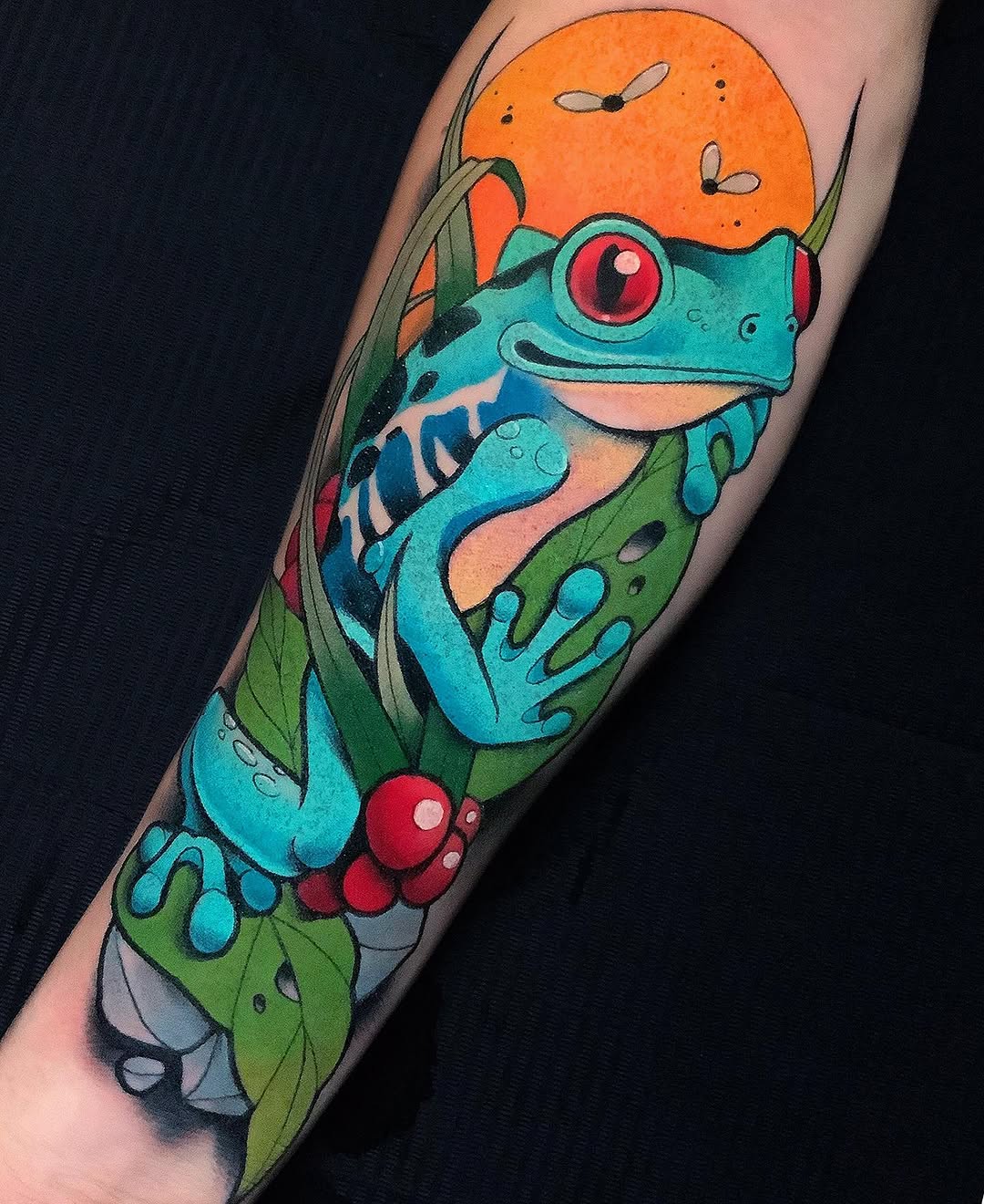 Colorful turquoise tree frog with red eyes and red toe pads, perched on green leaves with an orange sun and flying insects above, tattooed on a forearm.