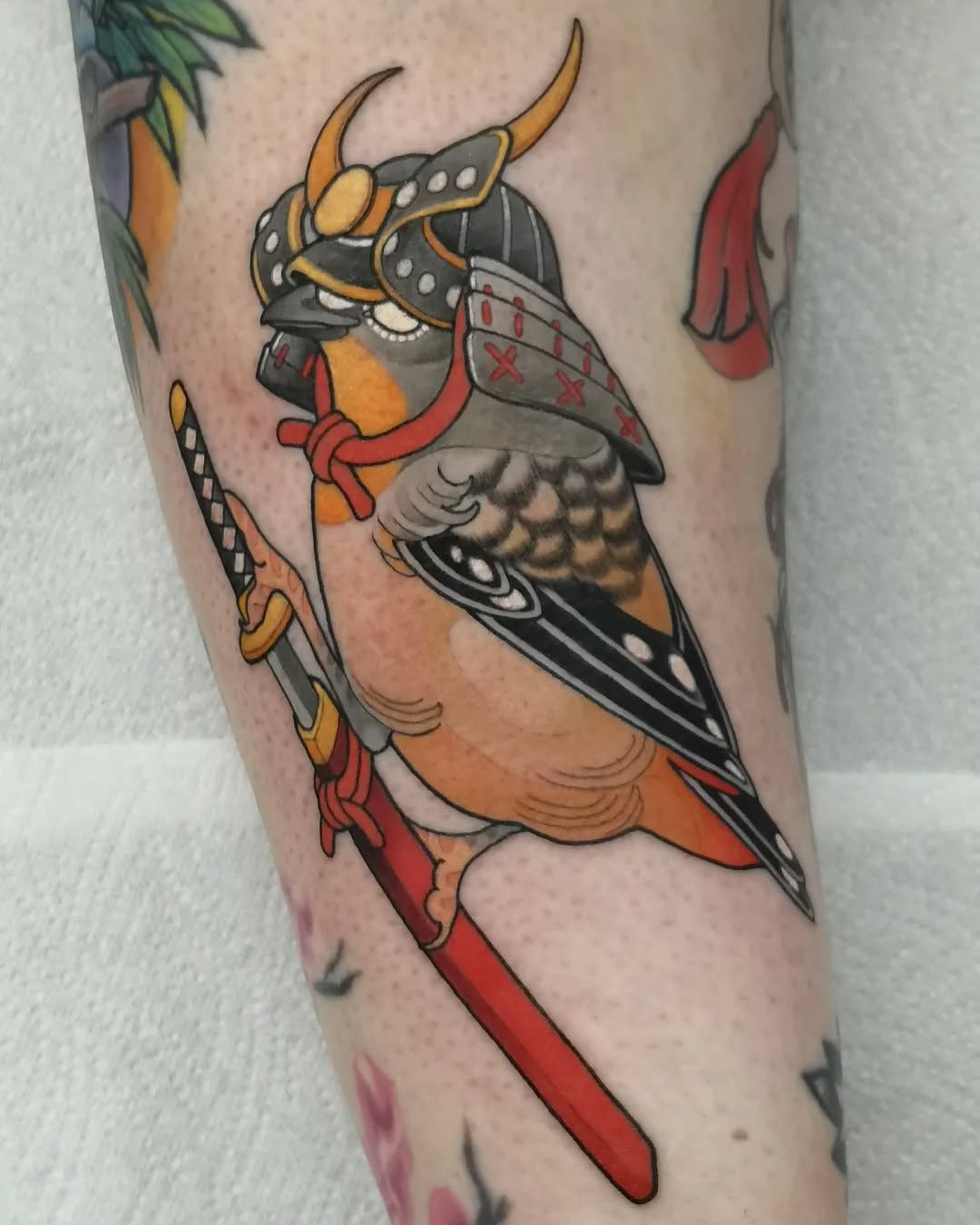 Colorful tattoo of a winged warrior character with horns, armor, and sword on the upper leg, featuring orange, red, black, and yellow hues.