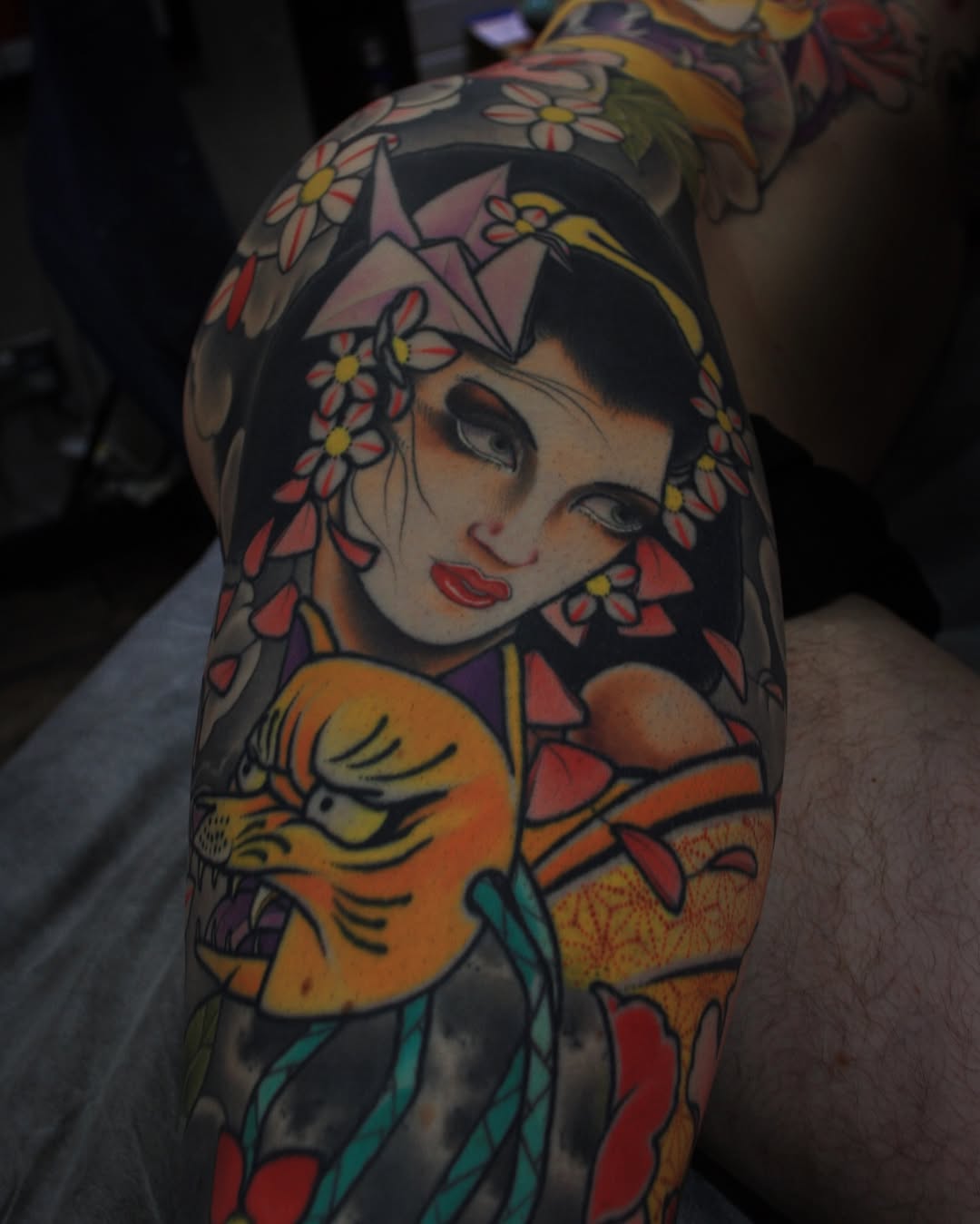 Colorful portrait tattoo of a woman's face with flowers in her hair and an orange bird on the upper arm, displayed on skin.