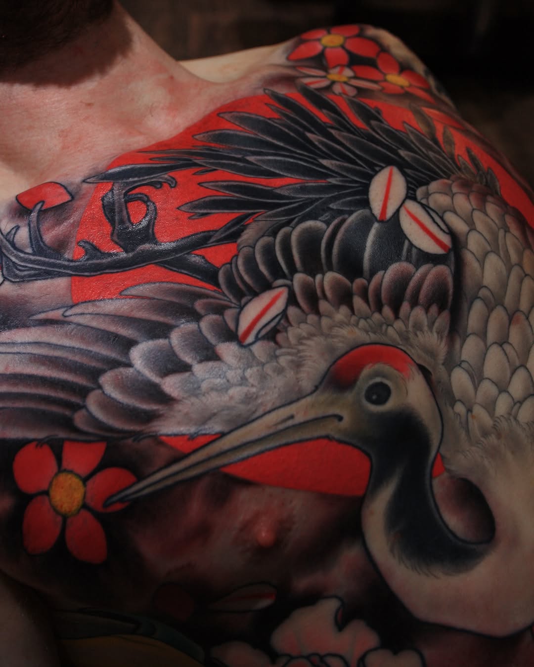 Colorful bird tattoo on hand featuring red flowers, black feathers, and detailed plumage in shades of tan, black, and red.