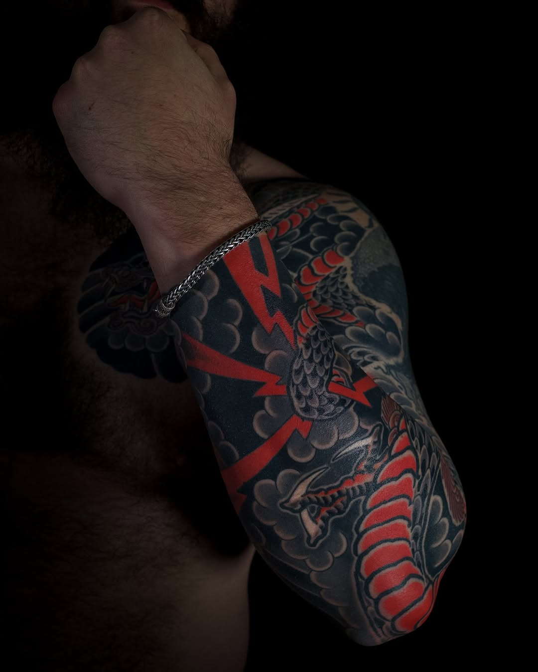 Man's arm and torso featuring a large tattoo with red lightning bolts, dark scales, and ornamental designs in red and dark blue ink.