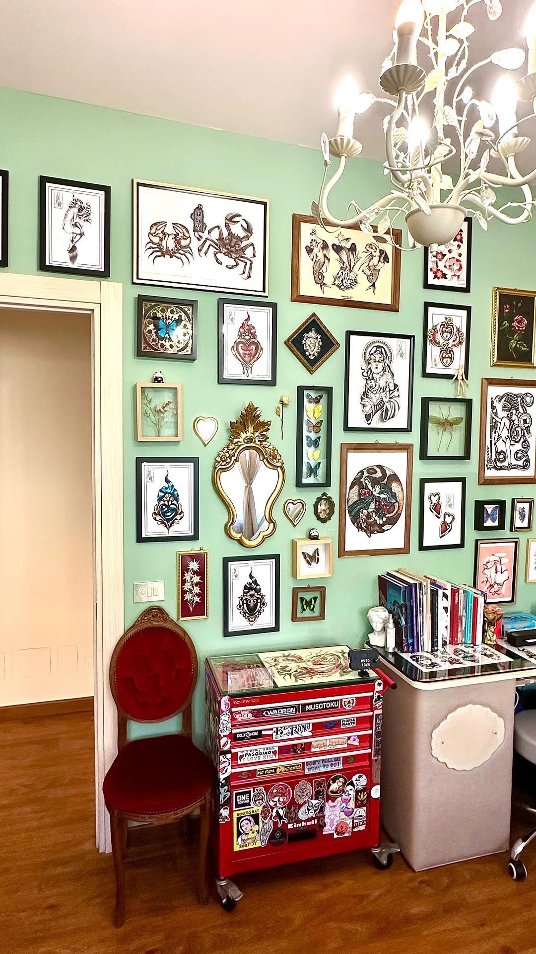 A gallery wall displays framed tattoo designs featuring hearts, crustaceans, flowers, and mystical imagery in various sizes against mint green walls.
