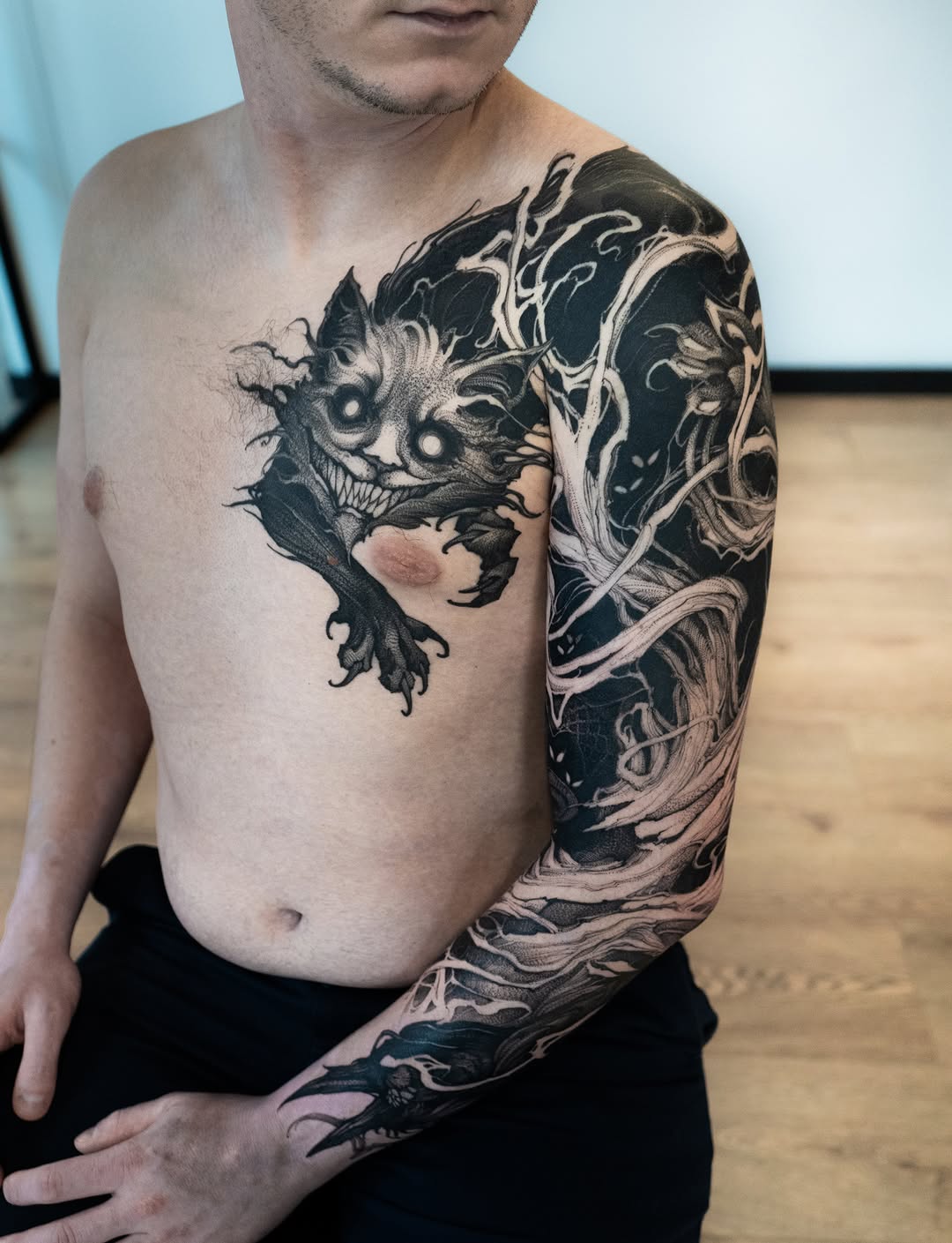 Shirtless man displaying a full right arm and chest tattoo featuring demonic creatures with ornate botanical elements in black and gray ink.
