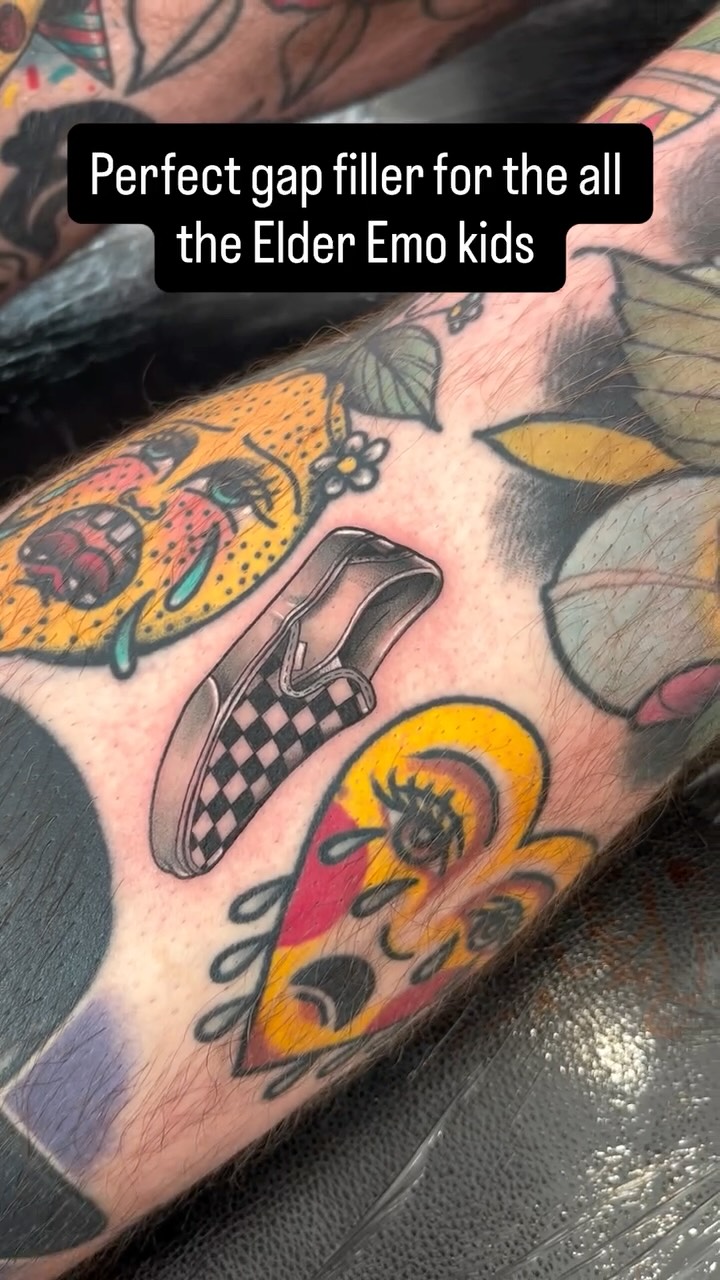 Colorful hand tattoo featuring a checkered shoe, butterflies, and floral elements in yellow, red, and orange on skin.