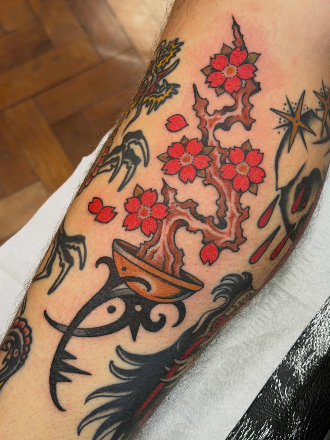Colorful arm tattoo featuring red flowers on a branching stem, a decorative mask, and various ornamental designs in red, black, and orange ink.