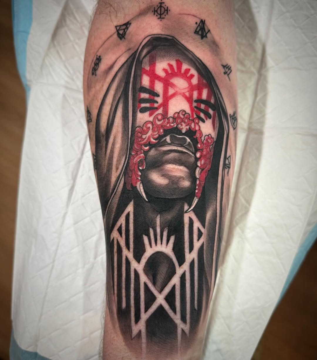 Hooded figure with red hair and facial markings on the upper leg, surrounded by small symbols and geometric patterns in black and red ink.