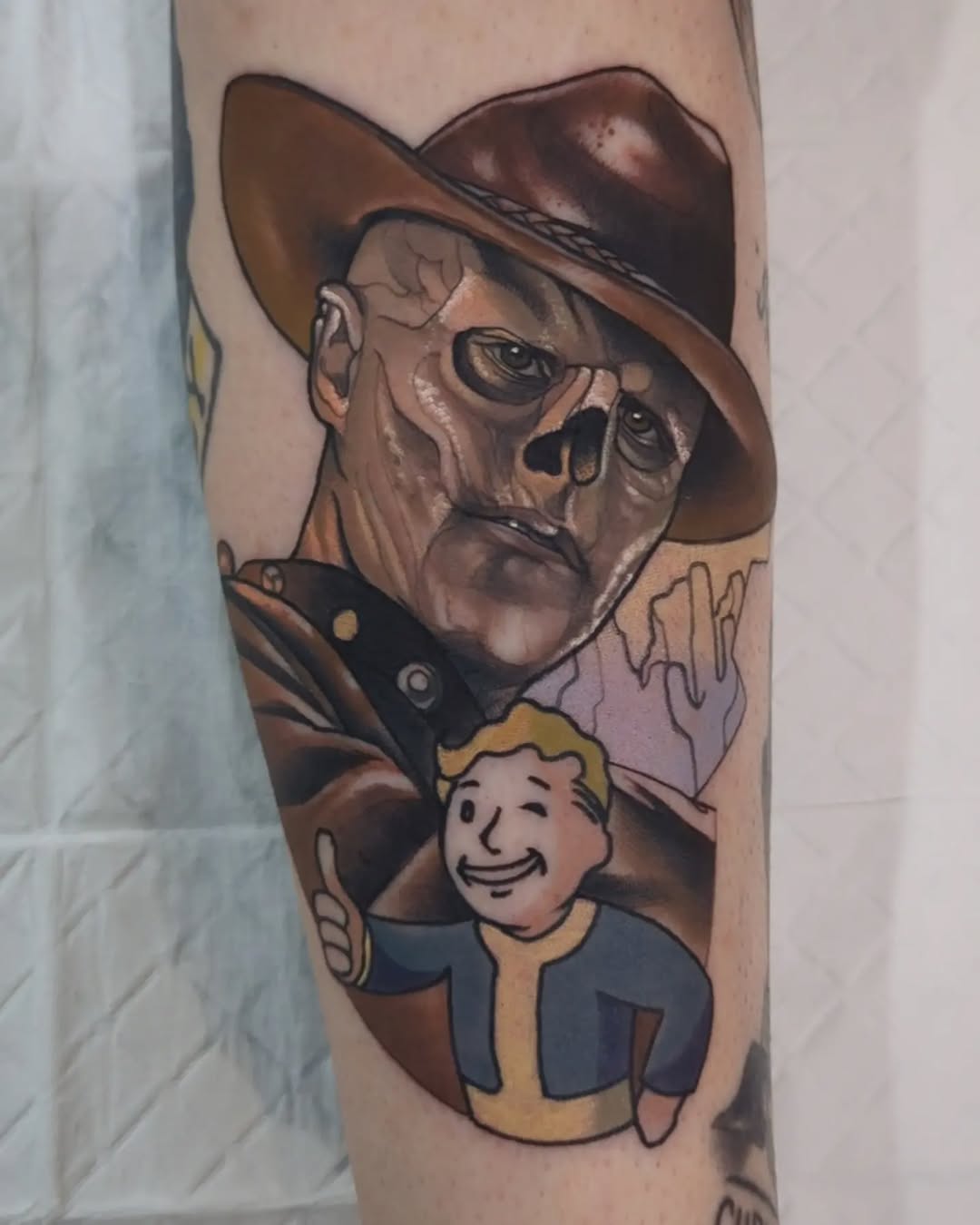Colorful arm tattoo featuring a skeletal cowboy in brown hat and sunglasses above a smiling blonde character in blue and yellow vault suit.