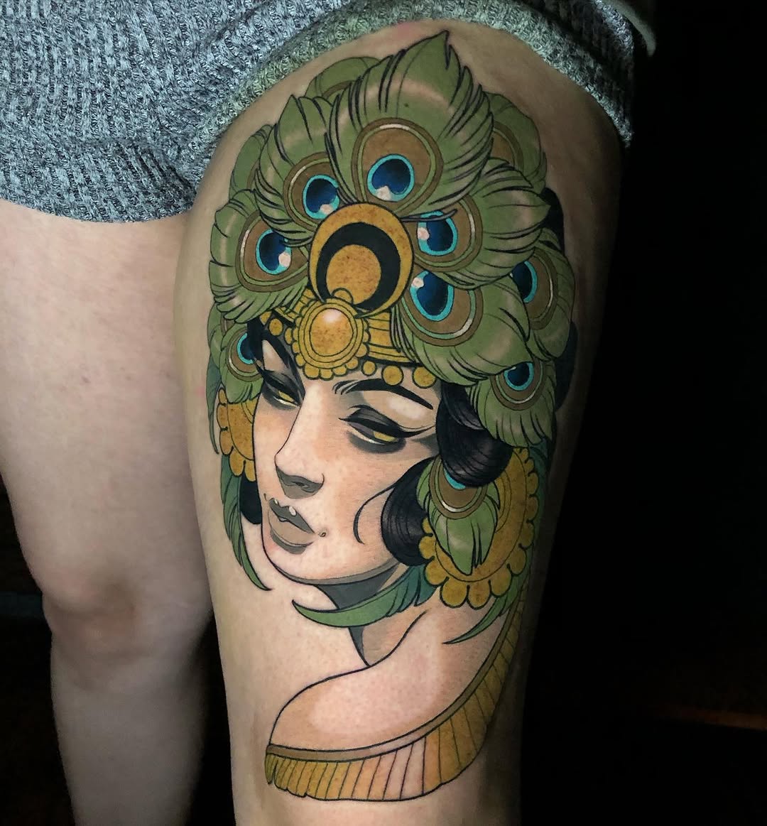 Woman's profile with closed eyes and peacock feathers forming her hair, rendered in green, gold, and blue on the upper thigh.