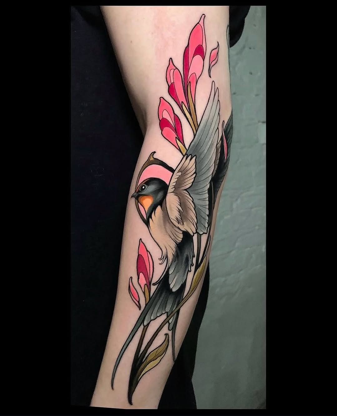 Bird with black and white wings and orange beak surrounded by pink and red flowering branches on inner forearm.