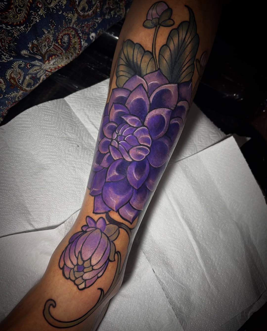 Purple lotus flowers with delicate wing details on the forearm, featuring shading and ornamental flourishes along the inner arm.