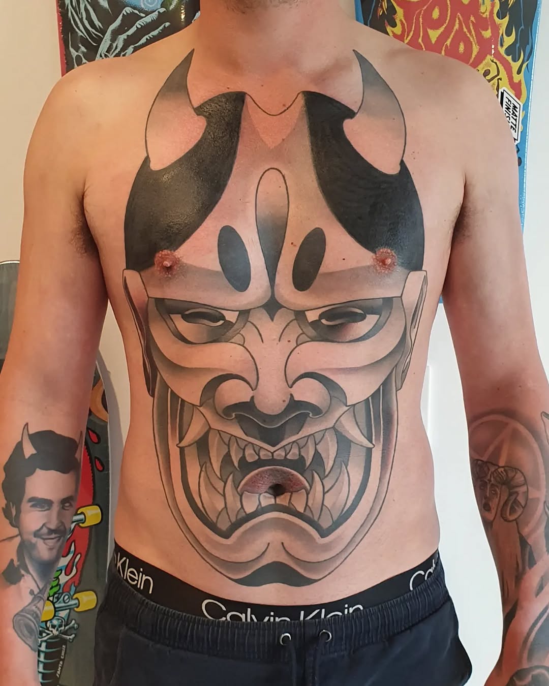Chest tattoo featuring a large demon or oni mask with horns, black shading, and intricate facial details in red and black ink.
