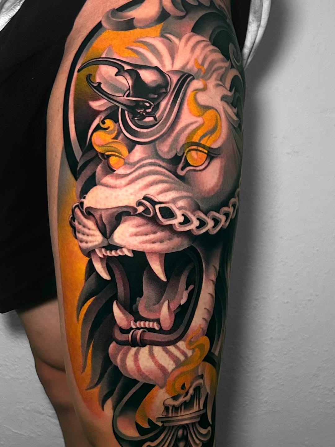 Colorful sleeve tattoo featuring stacked demon and skull faces with orange flames, ornamental details, and black outlines on the upper arm.