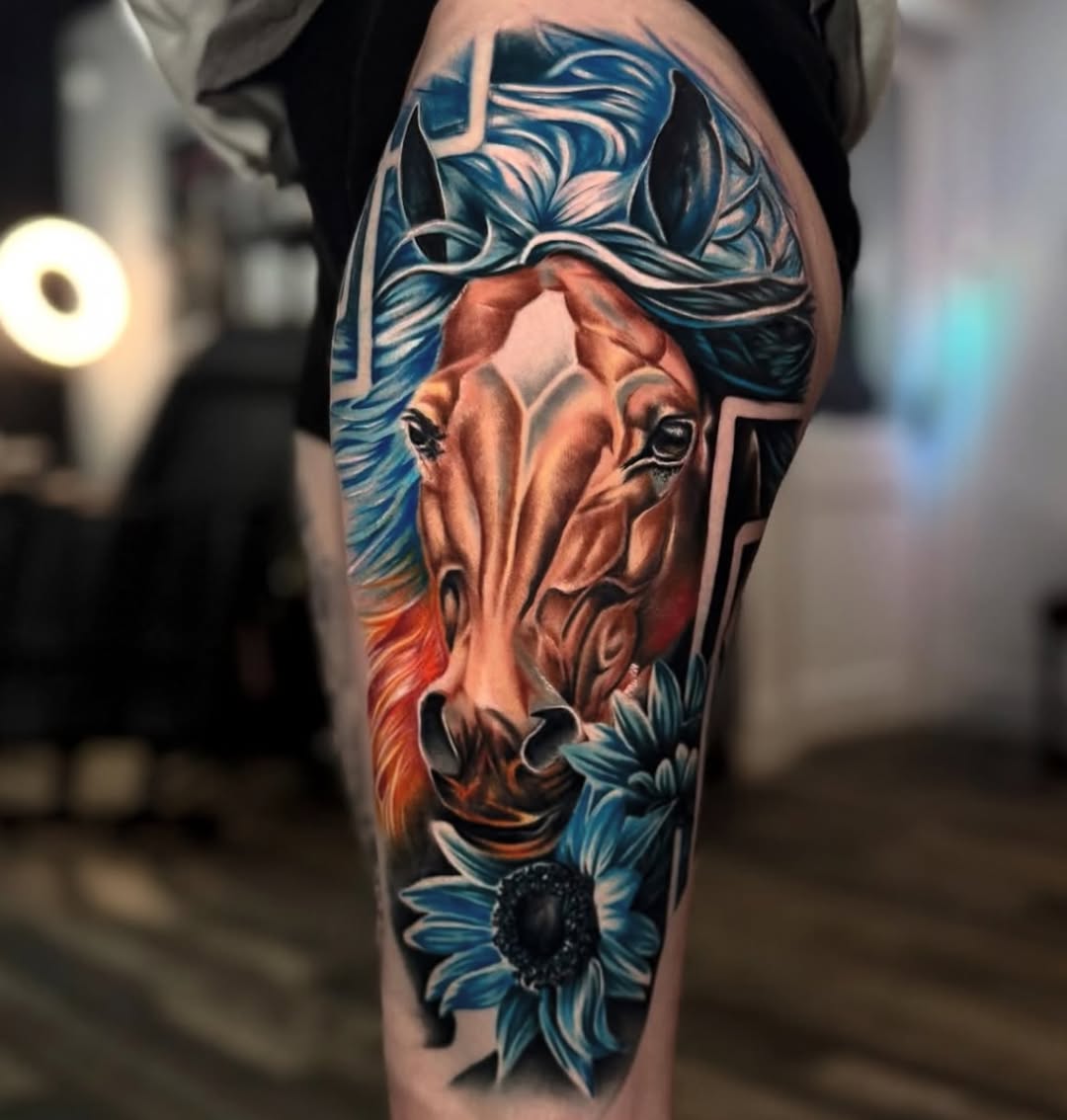 Colorful leg tattoo featuring a horse head with blue mane and orange tones, surrounded by blue flowers with detailed shading and highlights.