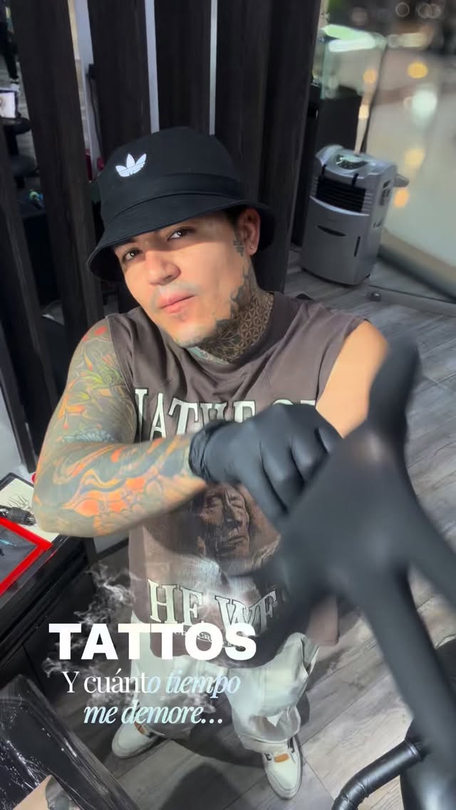 Tattooed person wearing black cap and sleeveless shirt displays colorful arm tattoo featuring orange and yellow design on their left sleeve.