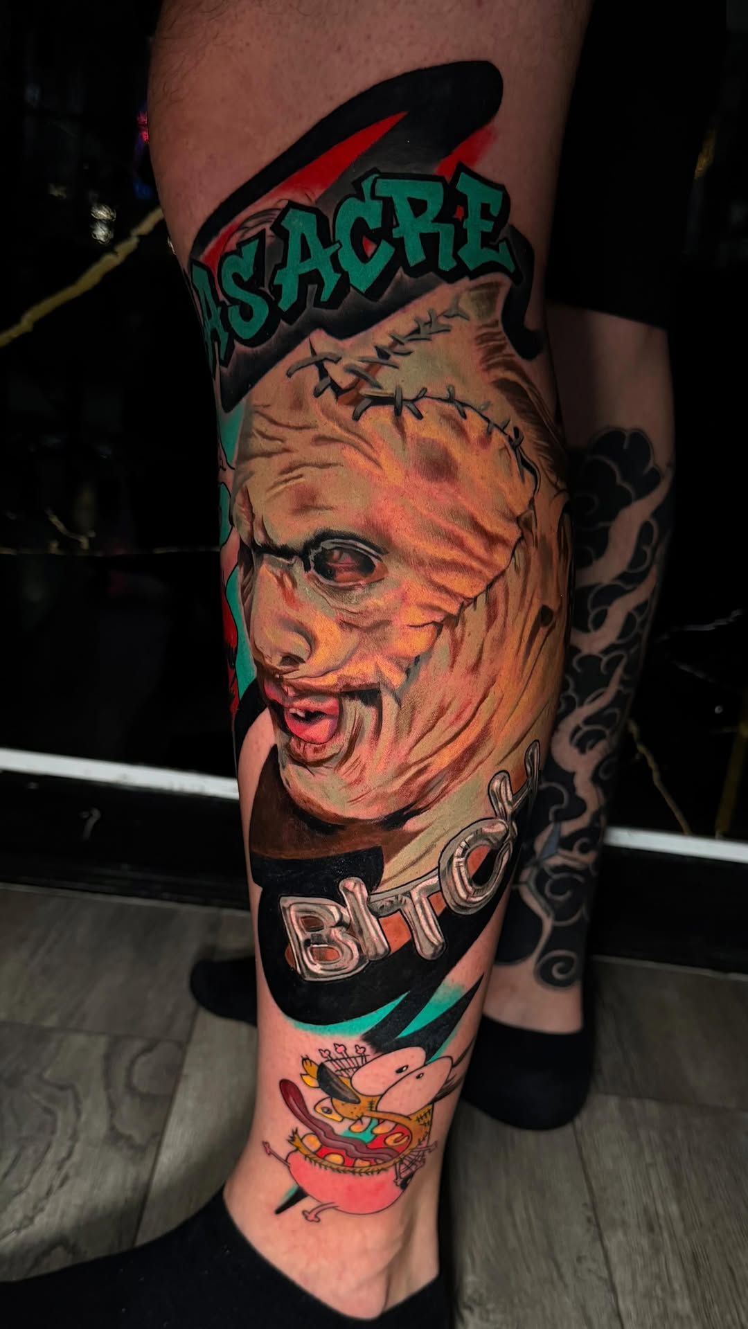 Colorful leg tattoo featuring a scarred face with "SLAUGHTER" text above and "BITO" below, surrounded by turquoise and red elements.