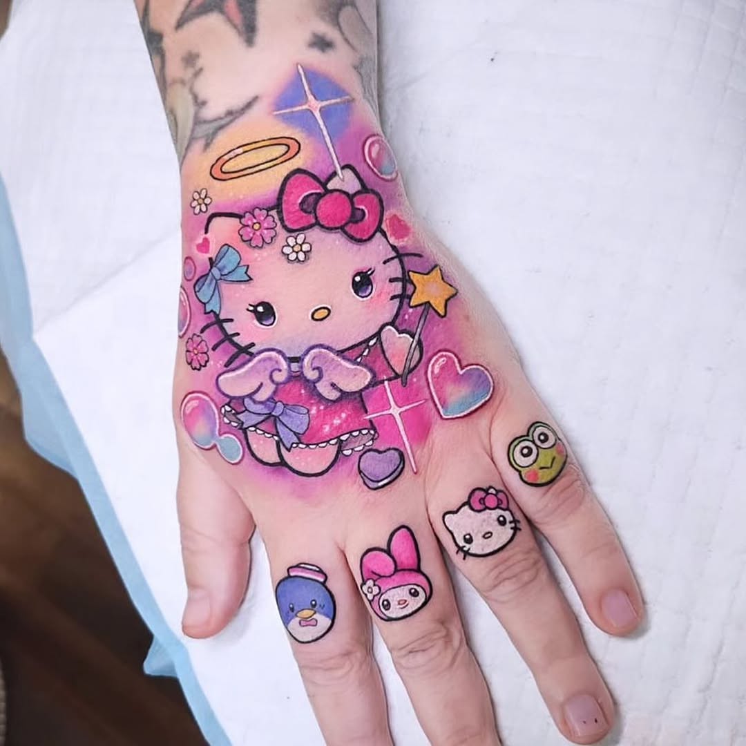 Colorful Hello Kitty angel tattoo on hand and fingers with hearts, flowers, stars, and celestial elements in pink, purple, and blue tones.